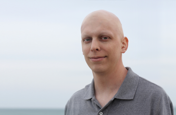 Smiling bald man standing in front of a body of water.